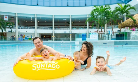 Rodzina w basenie strefy Jungle FUN, rodzice i dzieci na żółtym kole w parku wodnym z tropikalną roślinnością