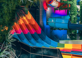 Colorful water slides at aquapark - orange-red and blue spiral slides surrounded by greenery