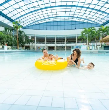 Czteroosobowa rodzina bawi się na żółtym pontonie w dużym basenie, w tle widoczne palmy i logo Jungle FUN.