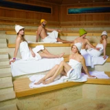 Group of friends relaxing in the Tropical SPA zone sauna, wearing traditional sauna hats and towel